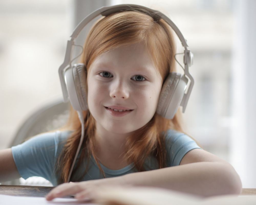 A young student wearing headphones and smiling while listening back to a recording