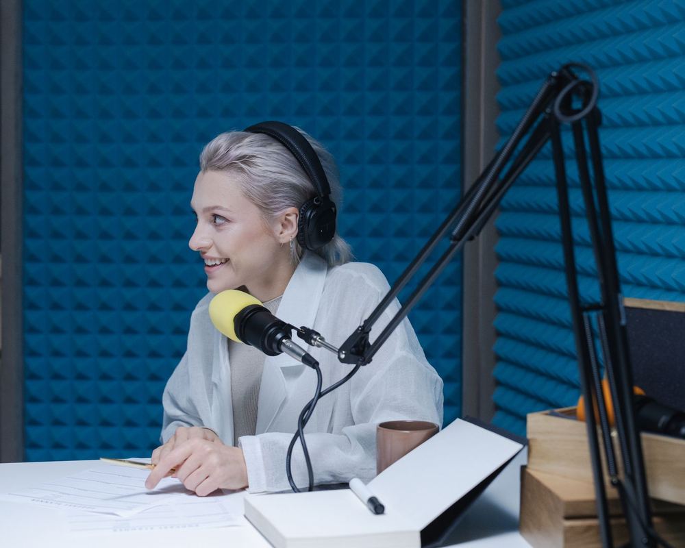 A teenager at the microphone during a live show, headphones on, acoustic panels behind