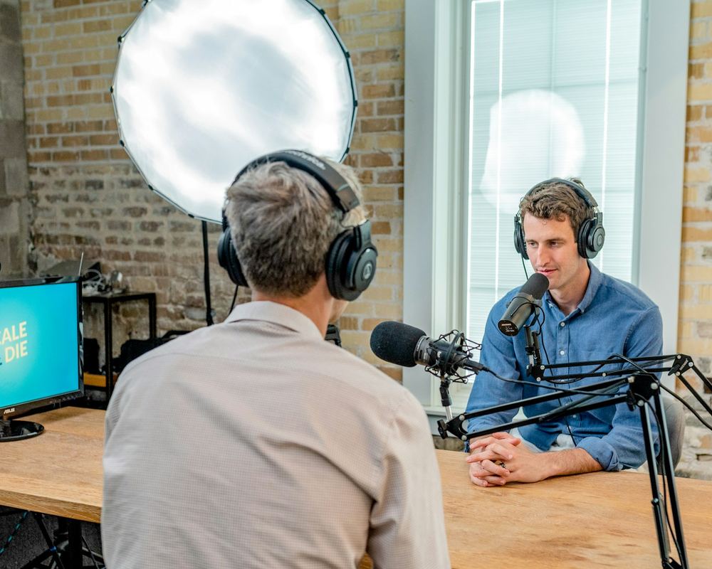 Two students talking across the microphones at a wooden studio desk