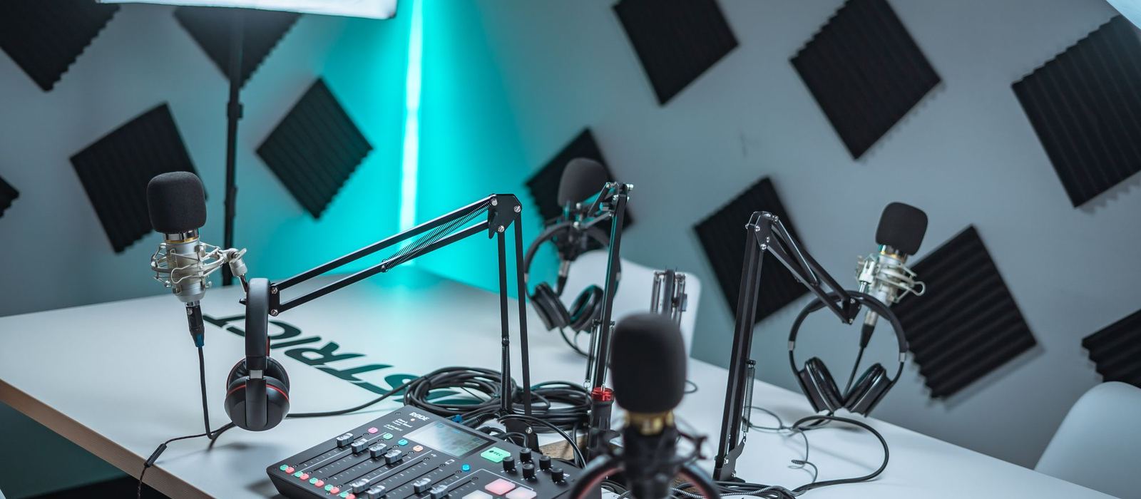 A small studio room with acoustic panels, three microphones on boom arms and a mixer